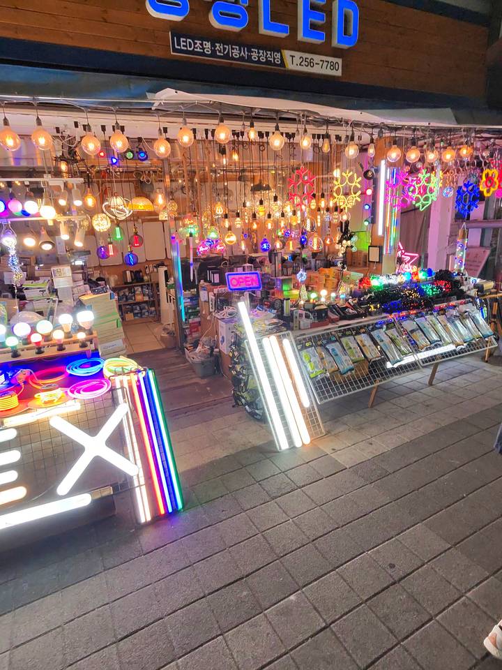 Vibrant market stall overflowing with colorful neon lights and electrical goods at night in Busan.