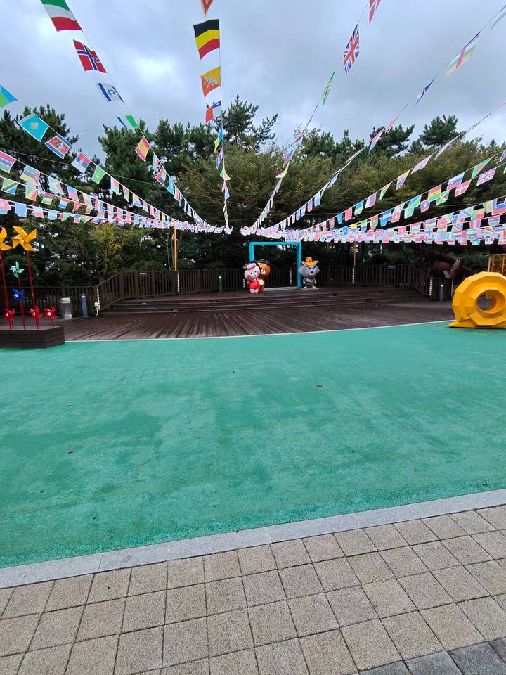 Empty outdoor stage with cartoon mascots and festive flags in a Korean city park.