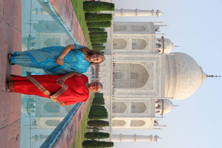 Two travellers dressed in colourful saris pose beside the Taj Mahal’s reflecting pool.