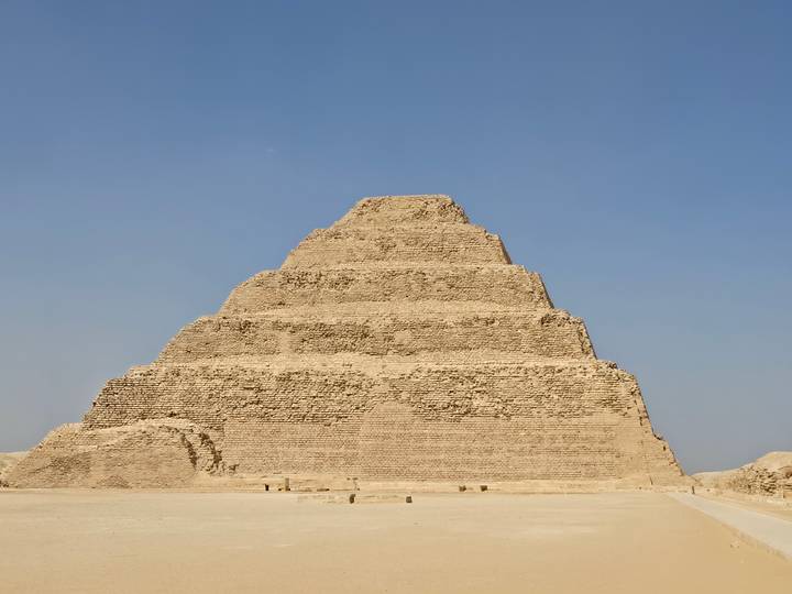 The Step Pyramid of Djoser rises in layers of weathered stone against a cloudless desert sky.