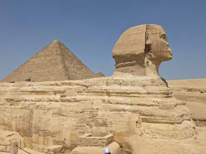 Profile of the Great Sphinx with the Pyramid of Khafre rising behind under a bright blue sky.