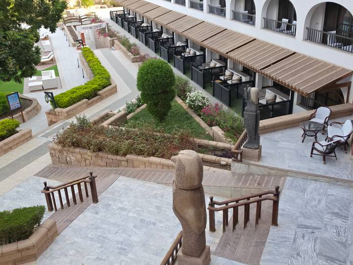 Terraced resort garden with stone statues, manicured hedges and balconies overlooking seating areas.