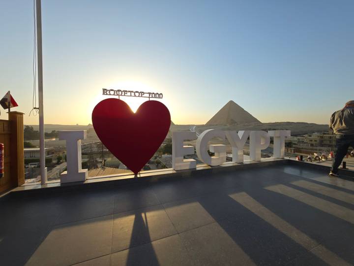 Sun sets behind a rooftop sign reading “I ♥ Egypt” with a pyramid silhouette in the distance.