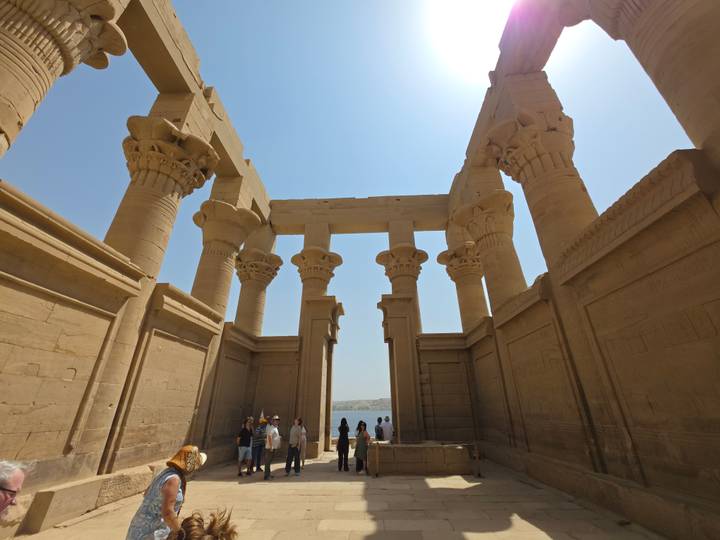 Sandstone colonnade of Philae Temple frames visitors exploring beneath a brilliant blue sky.