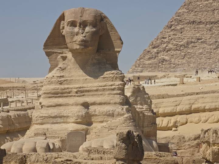 Close-up of the Great Sphinx’s weathered face with a pyramid and desert plateau behind.