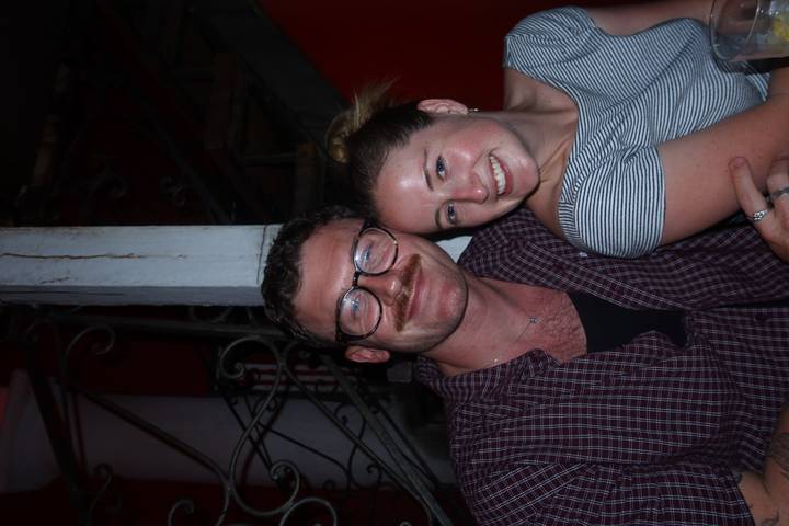 Close-up nighttime portrait of a smiling couple inside a dimly lit restaurant stairwell.