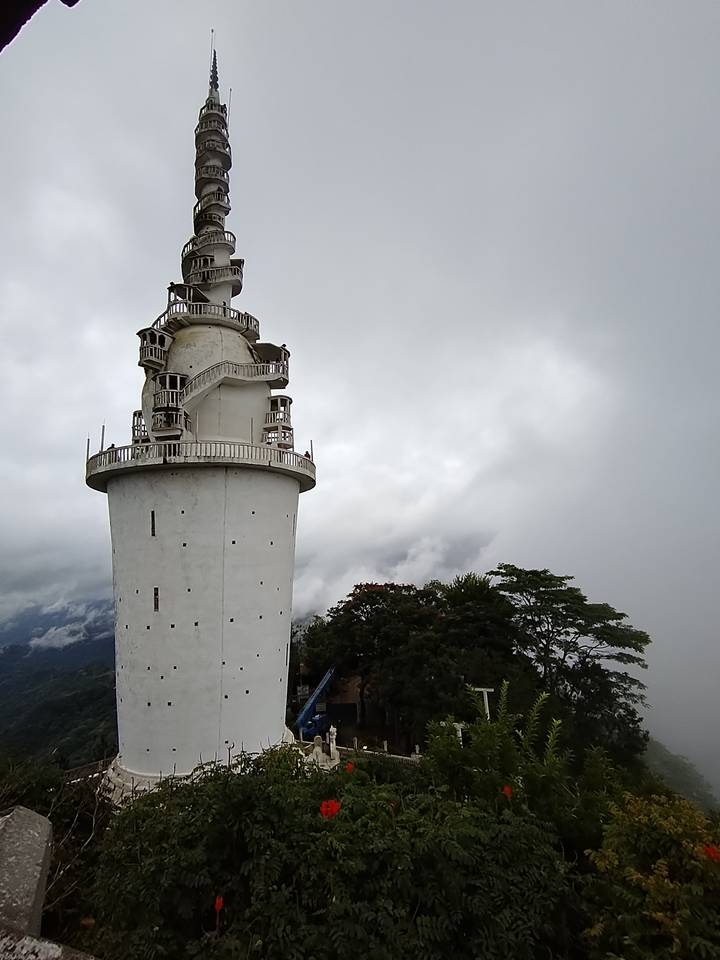 White cylindrical tower with spiral balconies rises against a cloudy mountain backdrop.