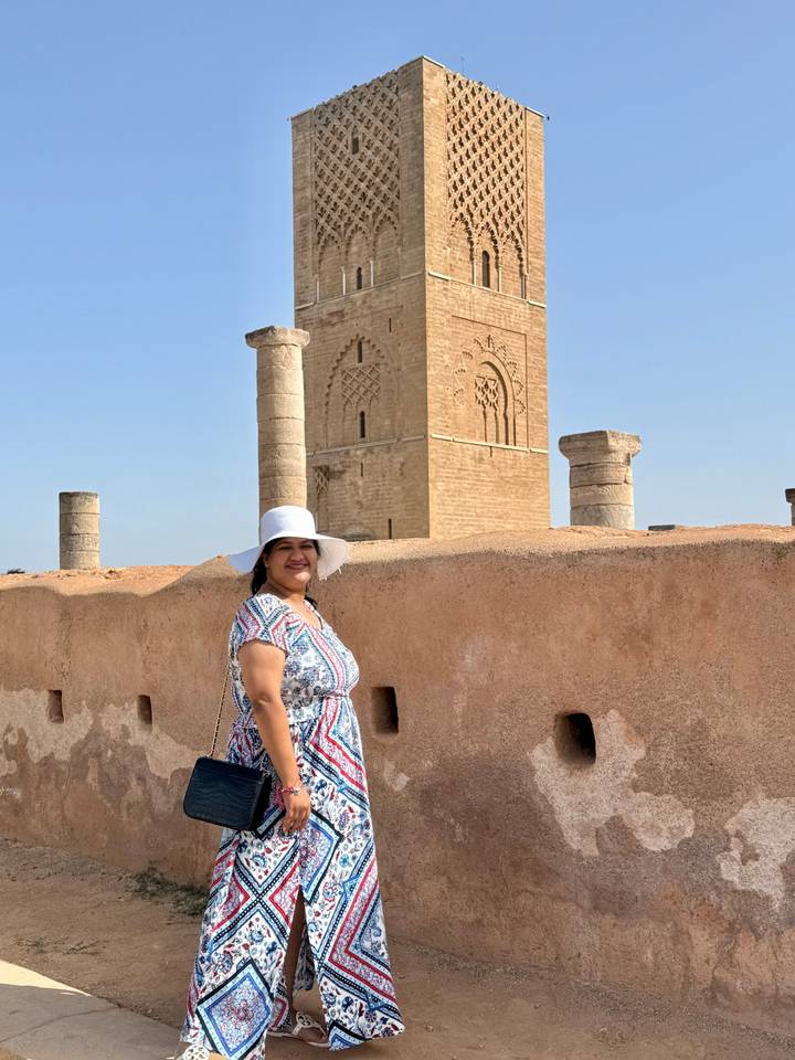Woman in sunhat smiles before the Hassan Tower ruins under clear blue sky.