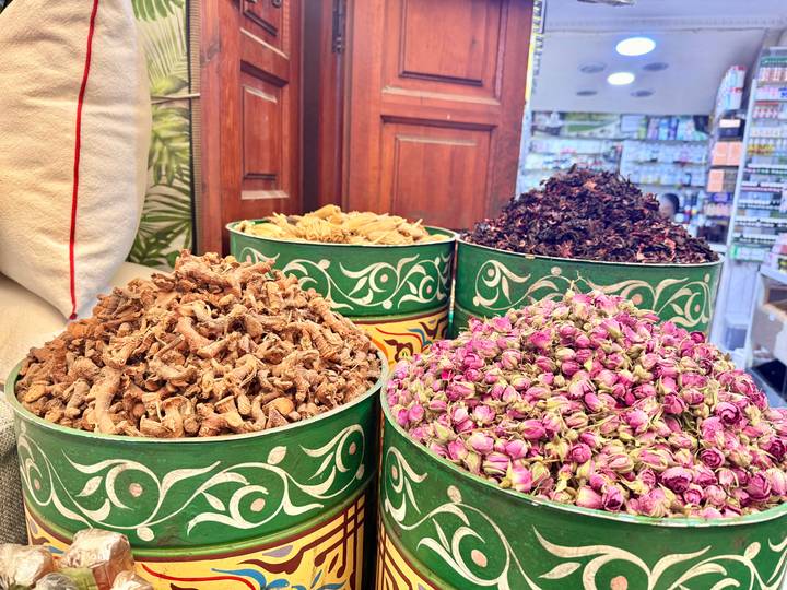 Buckets of dried Moroccan spices and rosebuds in a vibrant souk display.