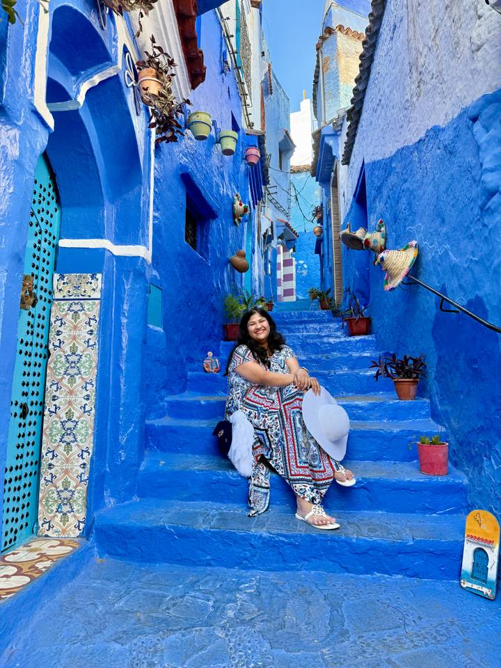 Woman sits on bright blue stairs amid pots and ceramics in Chefchaouen’s medina.