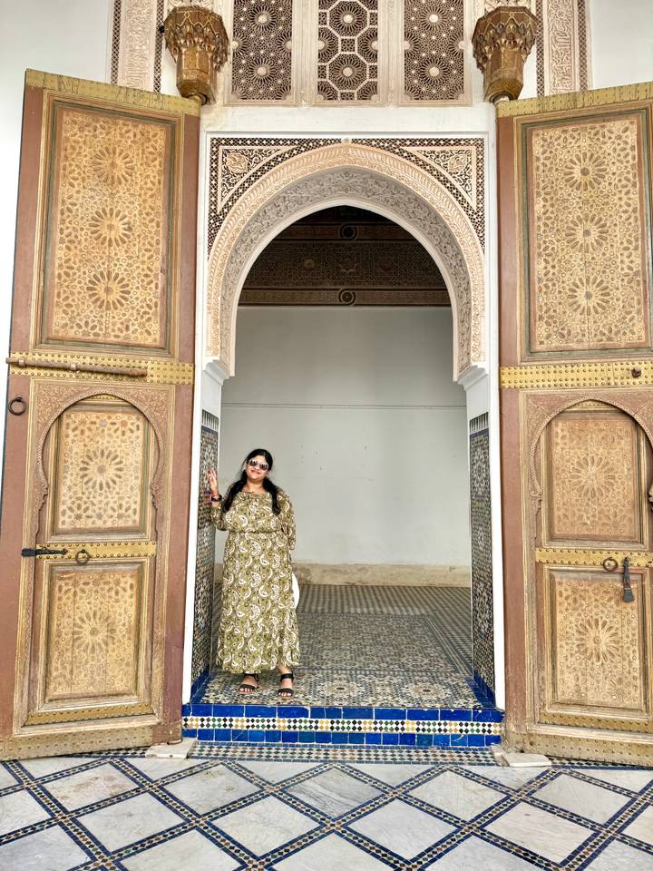 Visitor framed by ornate carved wooden doors and tiled panels in a Moroccan palace.
