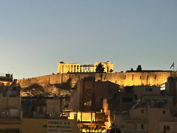 Evening view of the illuminated Parthenon atop the Acropolis rising above Athens rooftops.