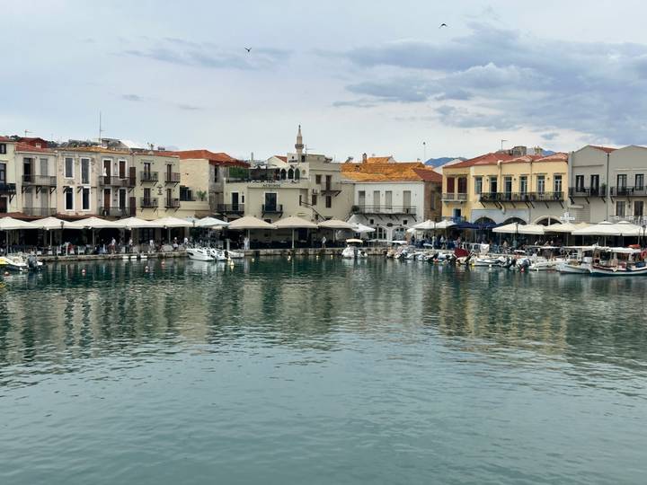 Picturesque Venetian harbor lined with pastel buildings reflecting in calm water under a mottled sky.