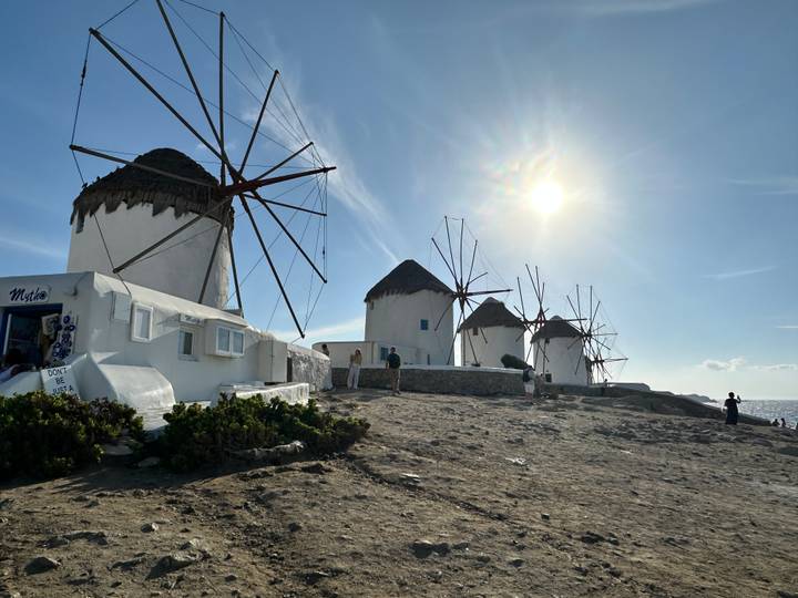 Iconic whitewashed windmills of Mykonos stand on a rocky bluff under bright afternoon sun.