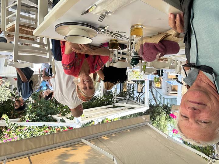 Casual open-air tavern scene with diners enjoying drinks beneath flowering bougainvillea canopy.