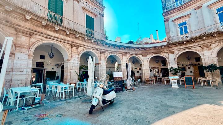 Circular arcade courtyard with café tables and a parked scooter under clear skies.