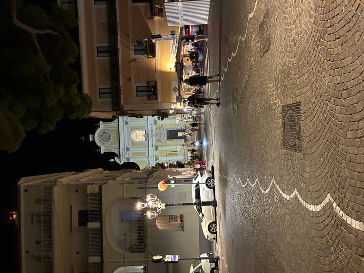 Evening street scene with a lit church at the far end and people strolling on cobblestone road.