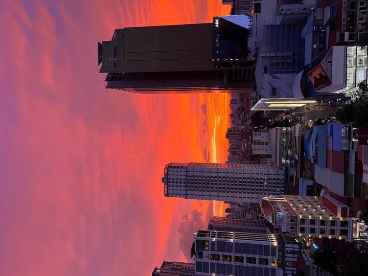 Vibrant pink and orange sunset sky above modern high-rise buildings of a bustling Asian city.