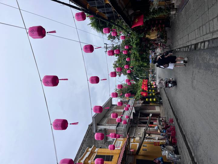 Quiet old-town street decorated with rows of bright pink lanterns hanging above stone pavement and heritage buildings.