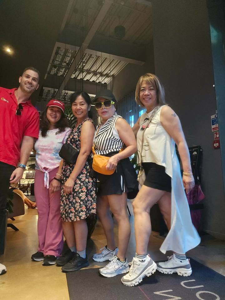 Group of travellers pose indoors with bright clothing and smiles near hotel reception.