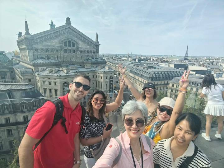 Cheerful selfie atop Parisian rooftop with Palais Garnier and distant Eiffel Tower in the background.