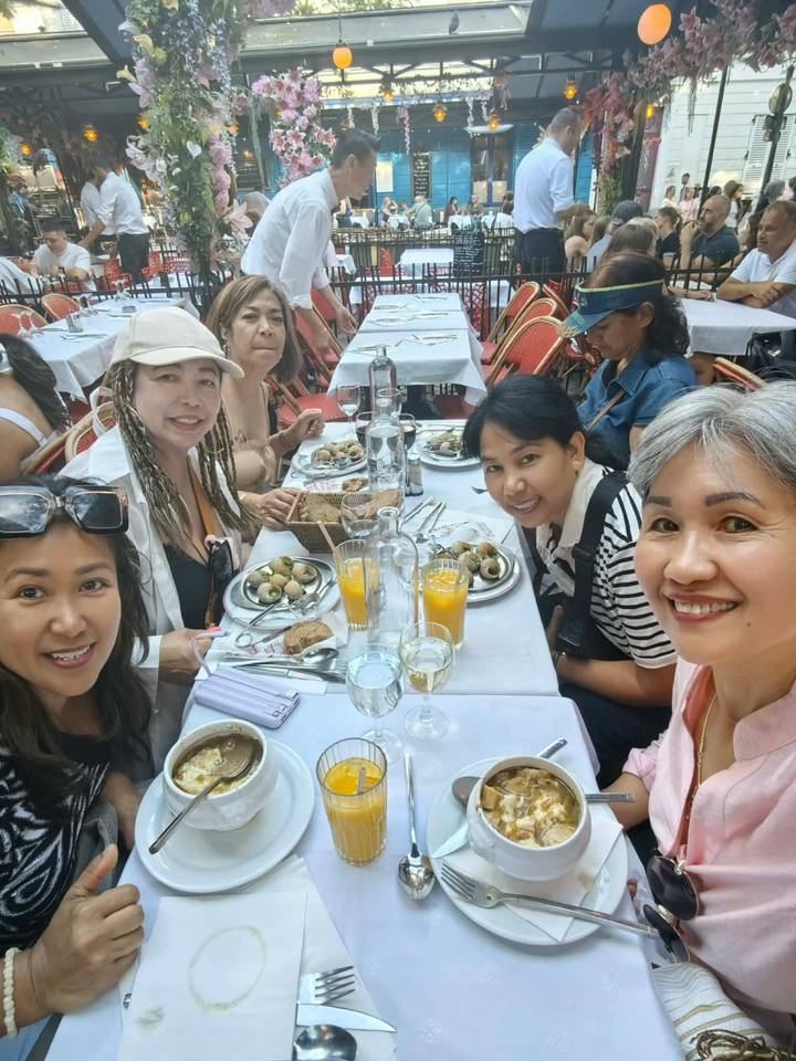 Friends share brunch at an outdoor Parisian café table with plates of eggs, bread and orange juice.