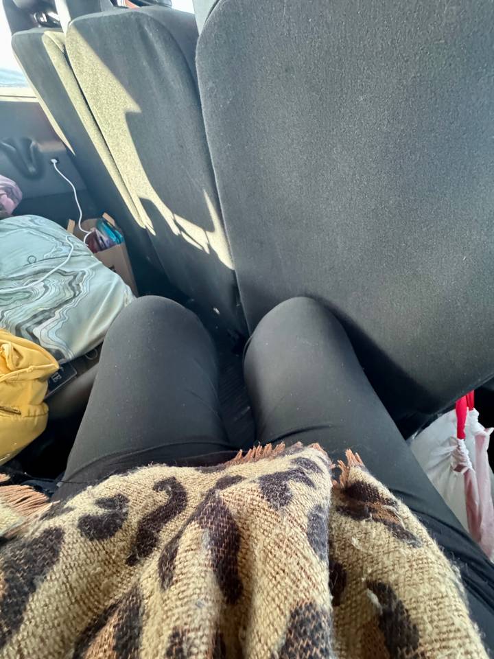 Casual snapshot of traveller’s knees in cramped vehicle seat with bags beside.