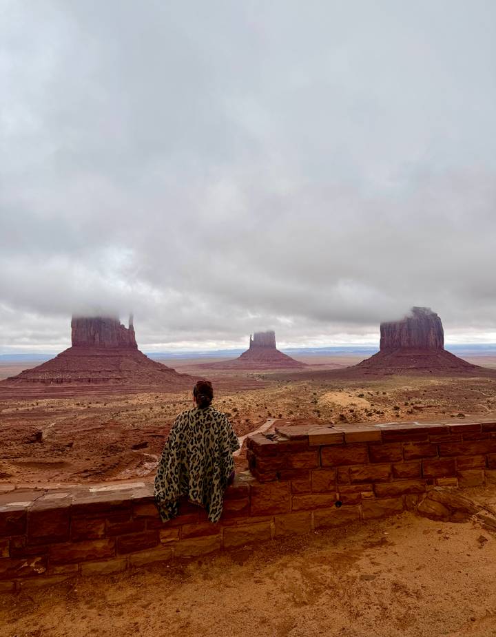 Visitor gazes at Monument Valley buttes partly shrouded by low clouds in vast desert.