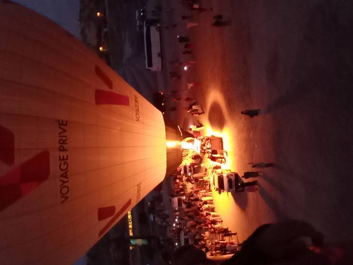 Hot-air balloon being inflated in the pre-dawn glow while crowds and support vehicles gather around.