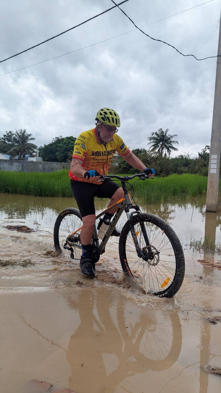 Cyclist rides through a flooded path with rice paddies and palm trees around.