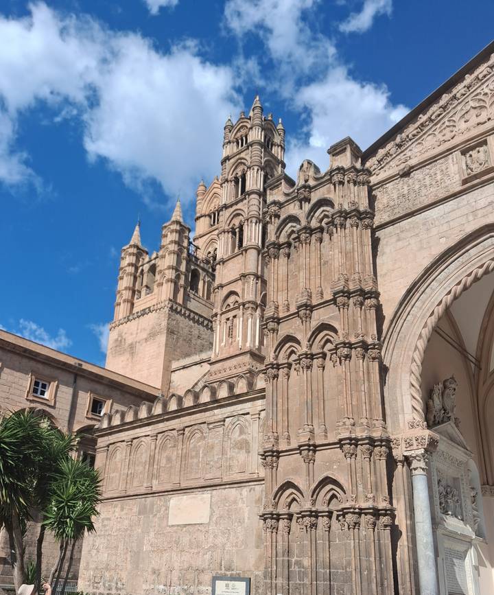 Detailed facade of Palermo Cathedral with its ornate towers and arches under bright blue sky.