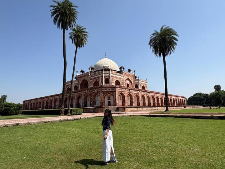 Woman posing in front of Humayun’s Tomb surrounded by palm trees and gardens.