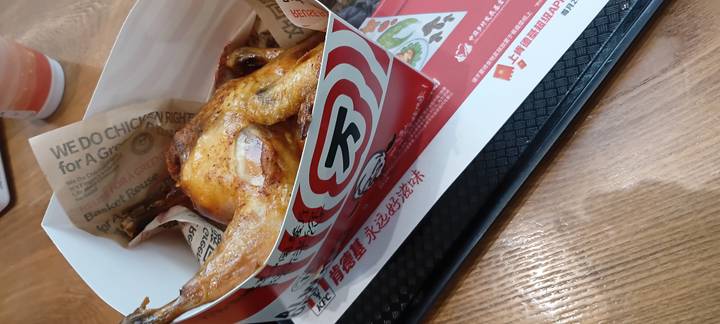 Fast-food style roasted chicken served in a branded paper box on a cafeteria tray.