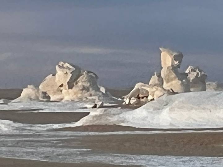 Blurred distant view of chalky rock formations topped with snow in a desert.