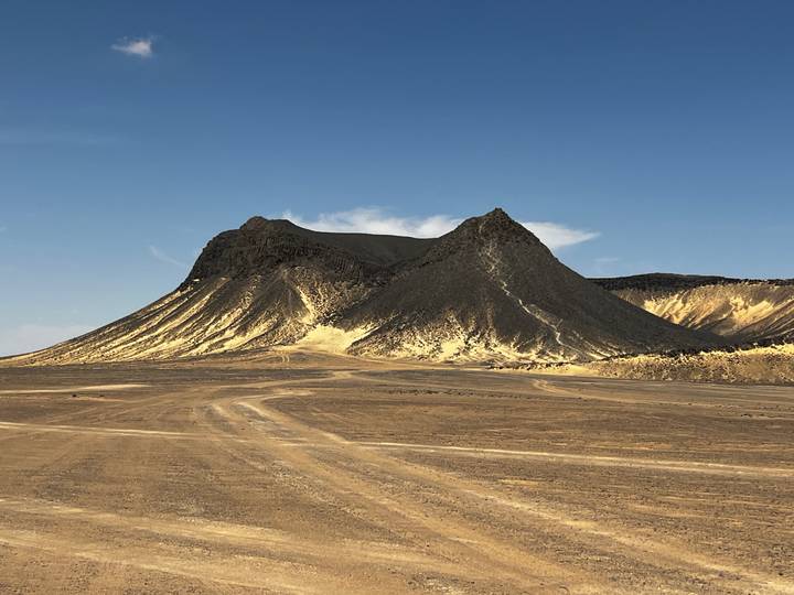 Dark volcanic cone with light sand streaks stands against a clear blue sky in Egypt’s Black Desert.