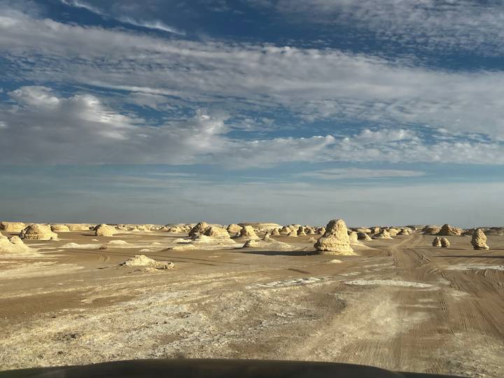 Expansive desert plain peppered with small chalk hoodoos under a textured blue sky.
