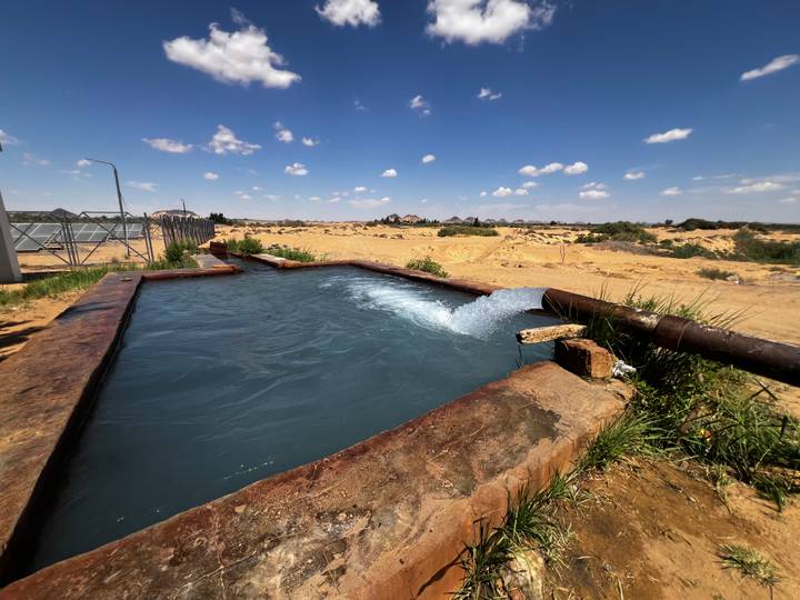 Rectangular outdoor hot spring pool with gushing water set amid sandy desert landscape.