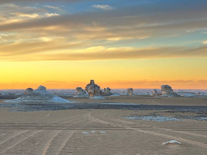 Golden sunset colors illuminate chalk spires across vast desert plain with soft clouds above.