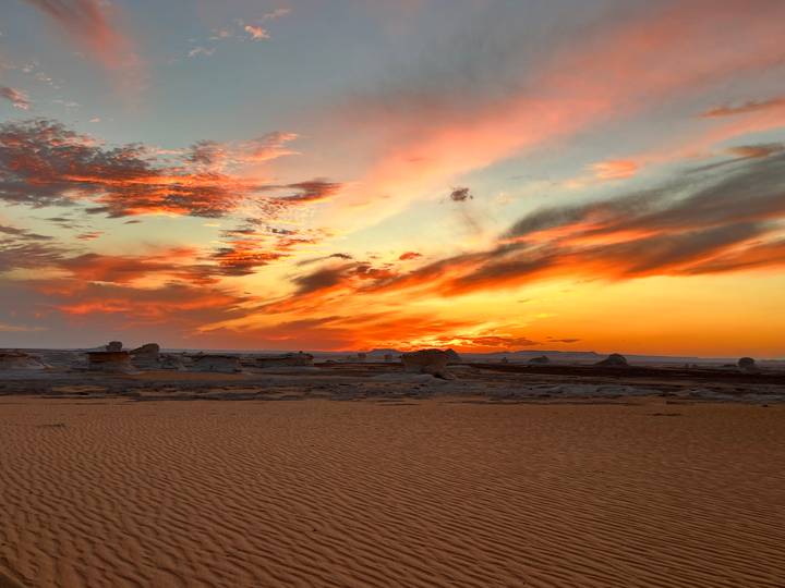 Vivid sunset over orange sand dunes and chalk rock formations in a remote desert landscape.