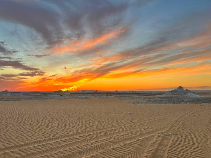 Fiery sunset paints streaks of orange and pink across the sky above rippled desert sand.