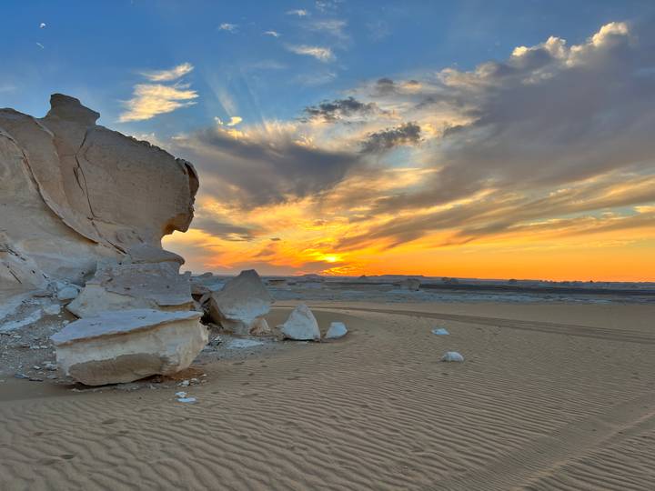 Golden sky behind dramatic chalk boulders and dune tracks during sunset in the desert.