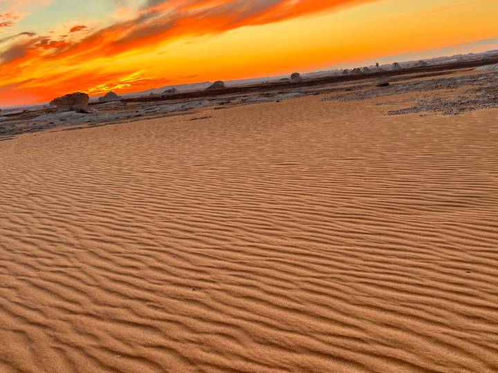 Close pattern of wind-rippled sand leading toward a vivid orange sunset on the horizon.