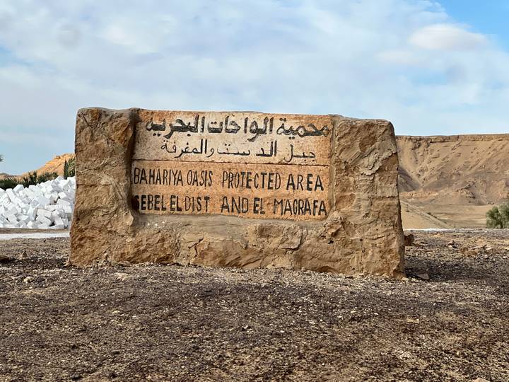 Stone marker announcing Bahariya Oasis Protected Area beside desert road.