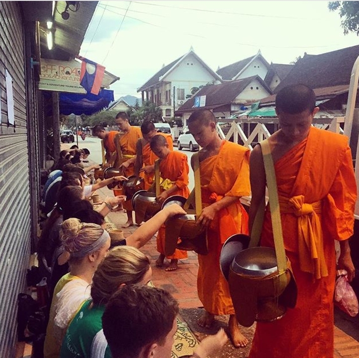 Monks receiving offerings from seated people on the street.