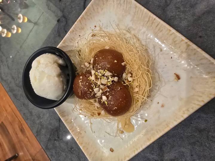 Plated Indian dessert of gulab jamun on crispy nest with a bowl of vanilla ice cream beside it