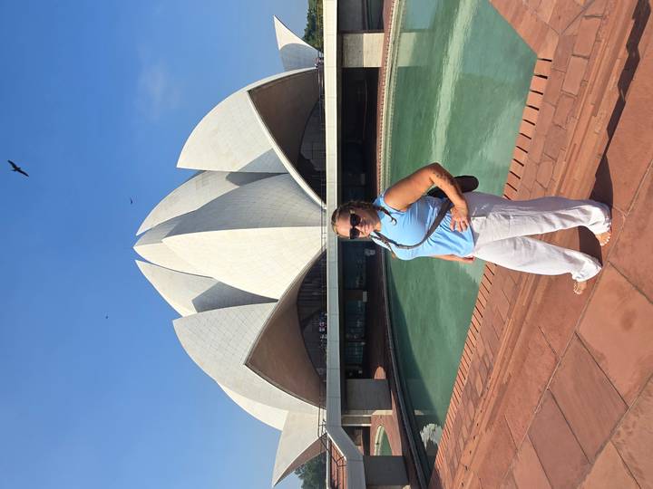 Traveller posing in front of the white-petaled Lotus Temple with reflecting pool under clear blue sky