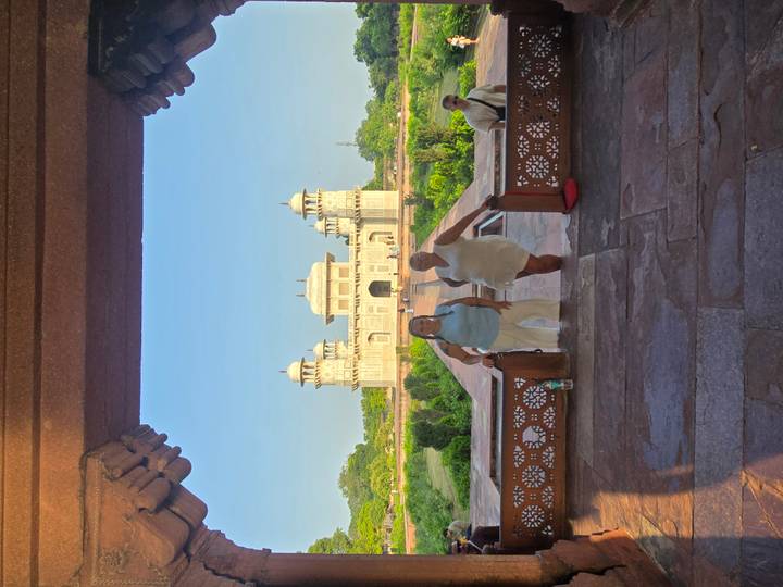 Two travellers posing on a shaded archway leading to the marble Baby Taj monument in Agra