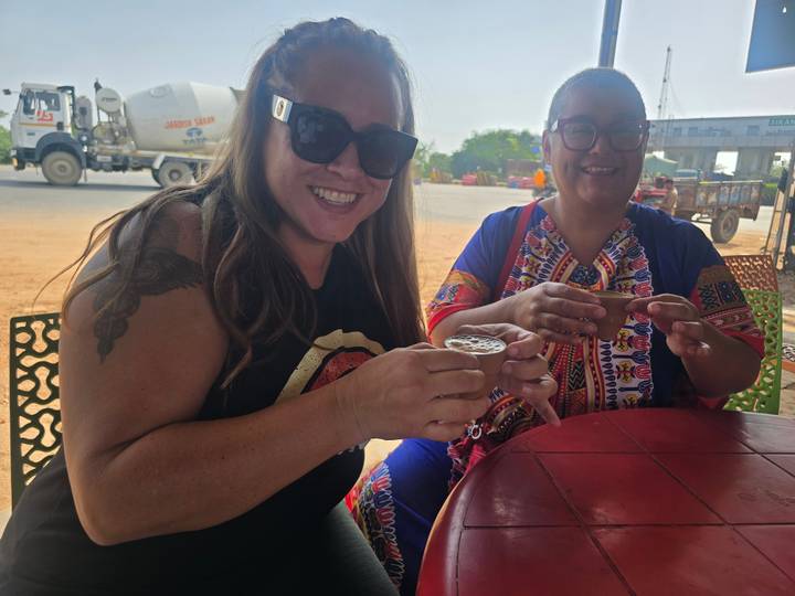 Two women enjoying roadside chai served in clay cups while seated at a small table