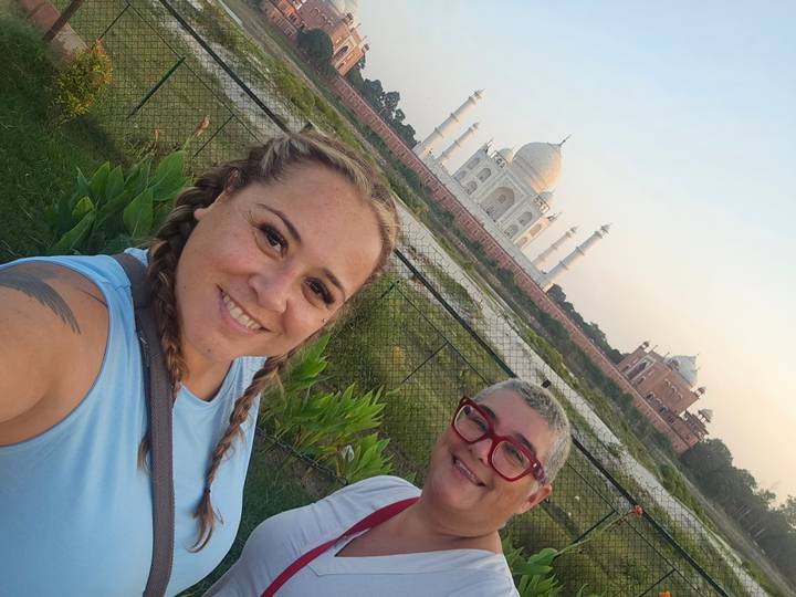 Selfie of two travellers in front of the Taj Mahal at soft evening light from riverside garden