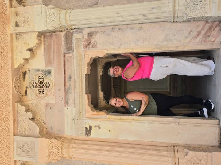 Two women strike playful poses in a narrow sandstone doorway of a historic Indian fort